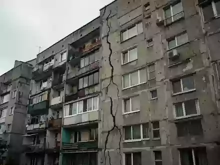 Ein mehrstöckiger Wohnblock mit deutlich sichtbaren Rissen in der Fassade bei bewölktem Himmel. - Foto: über boerse-global.de