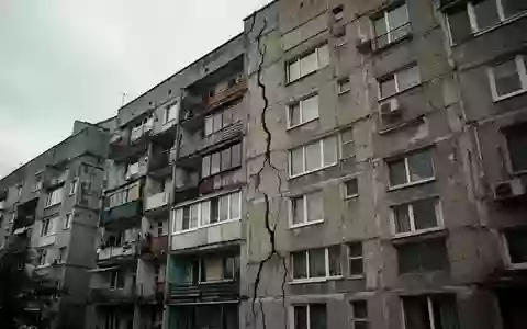 Ein mehrstöckiger Wohnblock mit deutlich sichtbaren Rissen in der Fassade bei bewölktem Himmel. - Foto: über boerse-global.de