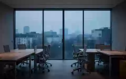 Ein minimalistisches, ruhiges Büro bei Dämmerung mit leeren Schreibtischen und Blick auf eine verschwommene Stadtlandschaft. - Foto: über boerse-global.de