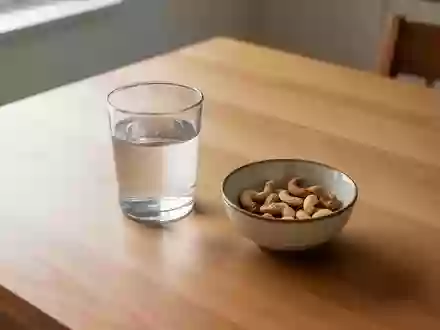 Ein schlichter Holztisch mit einem leeren Wasserglas und einer kleinen Schale mit Nüssen in einer ruhigen, hellen Umgebung. - Foto: über boerse-global.de