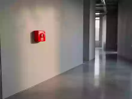 Ein roter Handfeuermelder an einer schlichten, grauen Wand in einem modernen Industriegebäude. - Foto: über boerse-global.de
