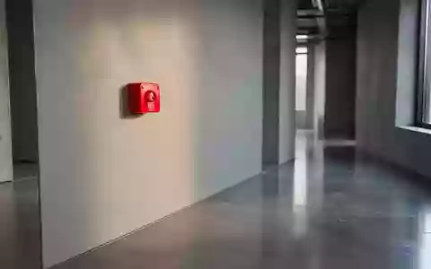 Ein roter Handfeuermelder an einer schlichten, grauen Wand in einem modernen Industriegebäude. - Foto: über boerse-global.de