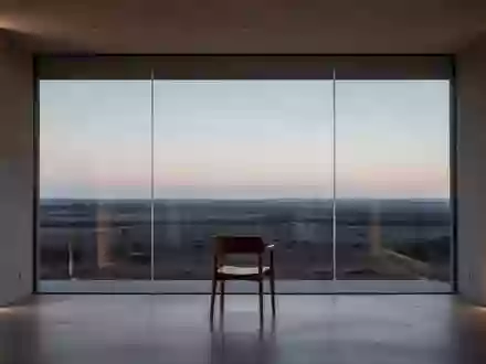 Ein minimalistischer, leerer Raum mit einem Stuhl vor einem großen Fenster, das auf eine weite Landschaft blickt. - Foto: über boerse-global.de