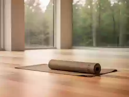Ein heller, minimalistischer Yoga-Raum mit Holzboden und Blick in einen ruhigen Wald, in dem eine zusammengerollte Yoga-Matte liegt. - Foto: über boerse-global.de