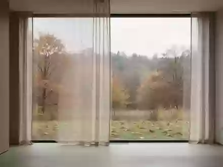 Ein minimalistischer Innenraum mit Blick auf eine sich wandelnde jahreszeitliche Landschaft durch ein großes Fenster. - Foto: über boerse-global.de