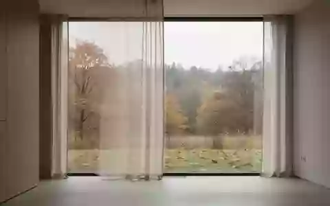 Ein minimalistischer Innenraum mit Blick auf eine sich wandelnde jahreszeitliche Landschaft durch ein großes Fenster. - Foto: über boerse-global.de