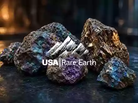 Nahaufnahme von glänzenden Seltenerdmineralien auf dunklem Stein vor einem stimmungsvollen, tiefblauen Hintergrund. - Foto: über boerse-global.de