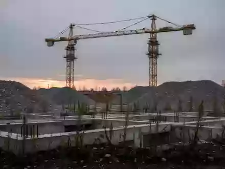 Eine verlassene Baustelle mit einem unbewegten Baukran und Betonfundamenten bei Dämmerung. - Foto: über boerse-global.de