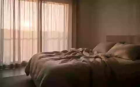 Ein minimalistisch eingerichtetes Schlafzimmer in ruhigem Morgenlicht mit ungemachtem Bett und neutralen Textilien. - Foto: über boerse-global.de