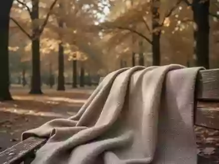 Ein strukturierter Wollstoff liegt auf einer Parkbank vor einem herbstlichen Hintergrund mit goldbraunen Bäumen. - Foto: über boerse-global.de
