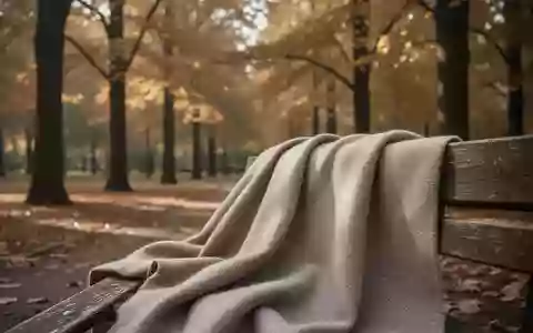 Ein strukturierter Wollstoff liegt auf einer Parkbank vor einem herbstlichen Hintergrund mit goldbraunen Bäumen. - Foto: über boerse-global.de