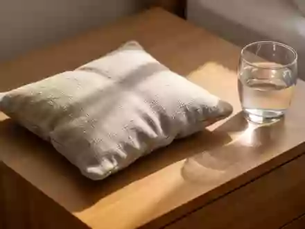 Ein Wärmekissen liegt auf einem Holztisch neben einem Glas Wasser in sanftem Morgenlicht. - Foto: über boerse-global.de