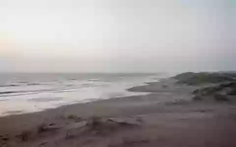 Eine ruhige, weitläufige Nordseeküste mit Dünen und flachem Wasser bei Dämmerung, die eine Atmosphäre der Stille vermittelt. - Foto: über boerse-global.de