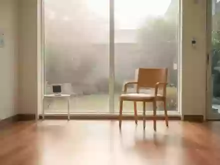 Ein heller, minimalistischer Rehabilitationsraum in einer modernen Klinik mit einem leeren Holzstuhl und Blick in einen Garten. - Foto: über boerse-global.de