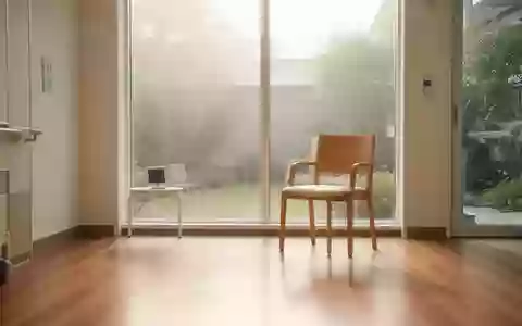 Ein heller, minimalistischer Rehabilitationsraum in einer modernen Klinik mit einem leeren Holzstuhl und Blick in einen Garten. - Foto: über boerse-global.de