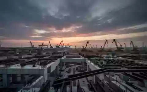 Eine weitläufige Baustelle für großflächige Infrastrukturprojekte bei Dämmerung mit massiven Betonfundamenten und Stahlträgern. - Foto: über boerse-global.de