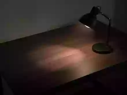 Ein minimalistischer, leerer Schreibtisch in einem dunklen Raum, beleuchtet von einer Schreibtischlampe, die lange Schatten wirft. - Foto: über boerse-global.de