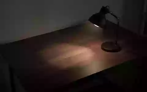 Ein minimalistischer, leerer Schreibtisch in einem dunklen Raum, beleuchtet von einer Schreibtischlampe, die lange Schatten wirft. - Foto: über boerse-global.de