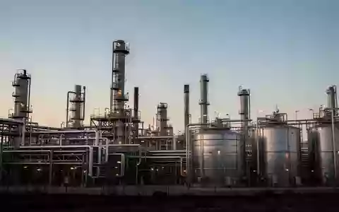 Industrielle Raffinerieanlage mit Stahlrohren und Speichertanks bei Dämmerung. - Foto: über boerse-global.de