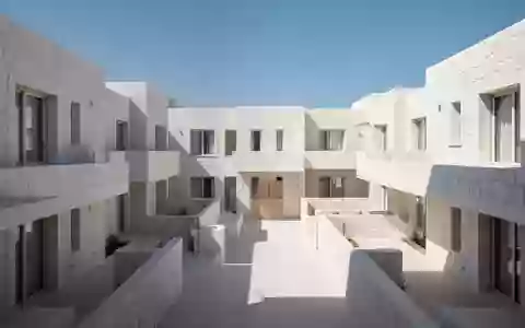Leerer Innenhof eines mediterranen Wohnkomplexes mit weißer Architektur und klaren Linien unter blauem Himmel. - Foto: über boerse-global.de