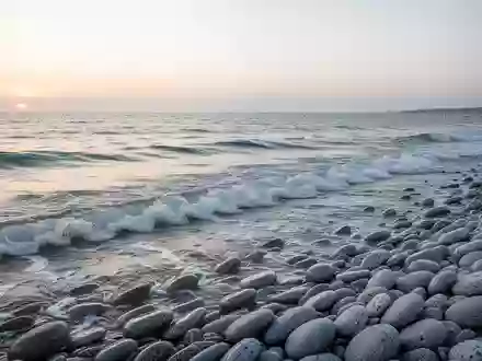 Eine ruhige Küstenlandschaft mit sanfter Brandung und glatten Kieselsteinen an einem Strand bei Tagesanbruch. - Foto: über boerse-global.de