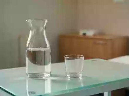 Ein heller, minimalistischer medizinischer Untersuchungsraum mit einem Glas Wasser auf einer weißen Oberfläche. - Foto: über boerse-global.de