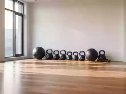 Ein minimalistischer Fitnessraum mit Holzboden, bei dem Hanteln und ein Medizinball ordentlich an einer weißen Wand stehen. - Foto: über boerse-global.de