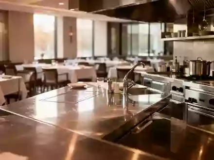 Eine moderne, unbesetzte Restaurantküche mit Edelstahlflächen und Blick in den Gastraum. - Foto: über boerse-global.de