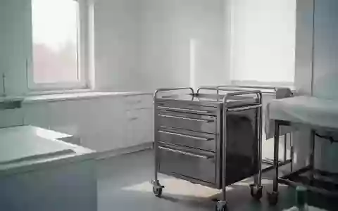 Ein steriler, minimalistischer Behandlungsraum in einer Klinik mit hellem Tageslicht und medizinischem Instrumentenwagen. - Foto: über boerse-global.de