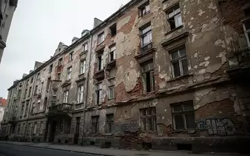 Verfallende Fassade eines Berliner Mietshauses mit bröckelndem Mauerwerk und sichtbaren Bauschäden an einem grauen Tag. - Foto: über boerse-global.de