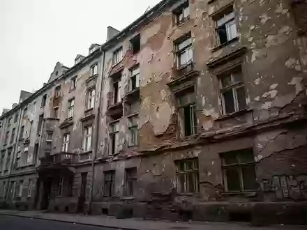 Verfallende Fassade eines Berliner Mietshauses mit bröckelndem Mauerwerk und sichtbaren Bauschäden an einem grauen Tag. - Foto: über boerse-global.de