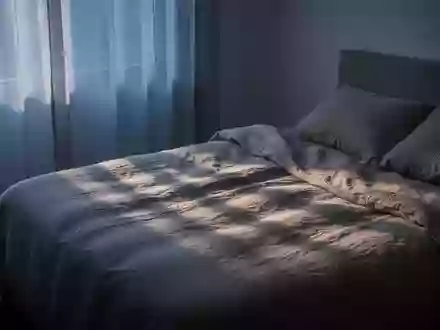 Ein minimalistisch eingerichtetes Schlafzimmer im sanften Licht der Morgendämmerung mit Fokus auf Texturen und Lichtstimmung. - Foto: über boerse-global.de