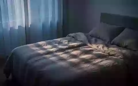 Ein minimalistisch eingerichtetes Schlafzimmer im sanften Licht der Morgendämmerung mit Fokus auf Texturen und Lichtstimmung. - Foto: über boerse-global.de