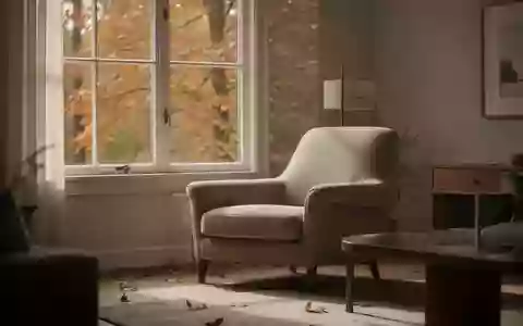 Ein ruhiges, sonnendurchflutetes Wohnzimmer im Herbst mit Blick auf herbstliche Blätter durch das Fenster. - Foto: über boerse-global.de