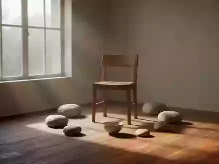 Ein ruhiger, minimalistischer Raum mit natĂĽrlichem Licht, einem leeren Holzstuhl und glatten Steinen auf dem Boden. - Foto: ĂĽber boerse-global.de