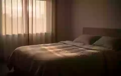 Ein minimalistisch eingerichtetes, ruhiges Schlafzimmer bei Tagesanbruch mit einem unbenutzten Bett und natürlichem Licht. - Foto: über boerse-global.de