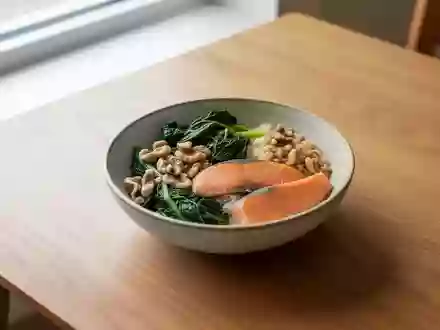 Eine Nahaufnahme einer ausgewogenen Mahlzeit mit grünem Gemüse, Nüssen und Lachs auf einem schlichten Holztisch bei Tageslicht. - Foto: über boerse-global.de