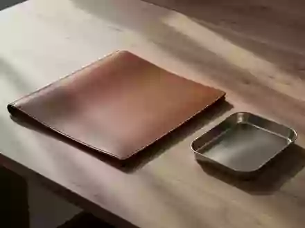 Ein minimalistischer Holzschreibtisch mit einer leeren Dokumentenmappe und einer Metallschale in natürlichem Licht. - Foto: über boerse-global.de