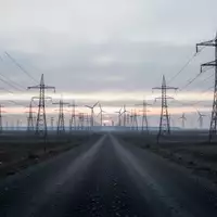 Weite Industrielandschaft mit Hochspannungsmasten und Windkraftanlagen bei Dämmerung unter einem bewölkten Himmel. - Foto: über boerse-global.de