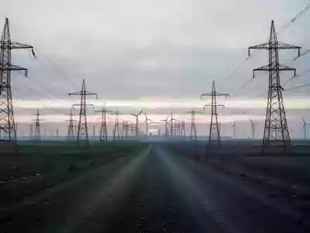 Weite Industrielandschaft mit Hochspannungsmasten und Windkraftanlagen bei Dämmerung unter einem bewölkten Himmel. - Foto: über boerse-global.de