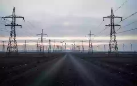 Weite Industrielandschaft mit Hochspannungsmasten und Windkraftanlagen bei Dämmerung unter einem bewölkten Himmel. - Foto: über boerse-global.de
