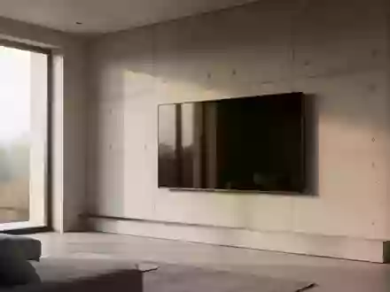Ein minimalistisch eingerichtetes Wohnzimmer mit einem an einer Betonwand montierten, ausgeschalteten Fernsehbildschirm. - Foto: über boerse-global.de