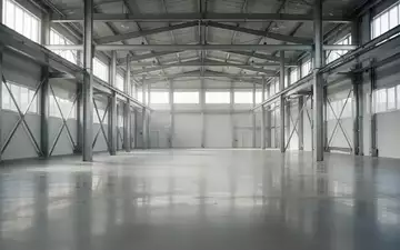 Helle, leere Industriehalle mit poliertem Betonboden und Stahlträgern in einer minimalistischen Architektur. - Foto: über boerse-global.de