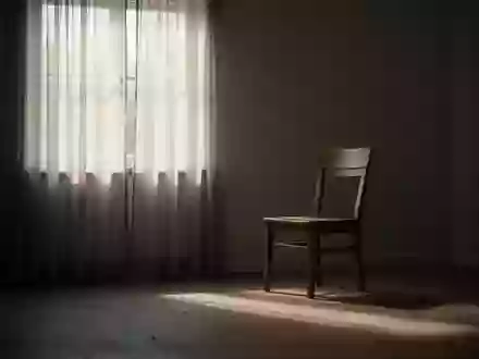 Ein einsamer, leerer Stuhl in einem ruhig beleuchteten Wohnzimmer am Fenster, der eine Atmosphäre der Isolation vermittelt. - Foto: über boerse-global.de