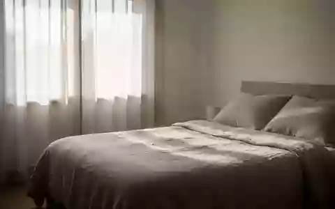 Ein minimalistisch eingerichtetes Schlafzimmer am frühen Morgen mit einfallendem Tageslicht auf einem bezogenen Bett. - Foto: über boerse-global.de