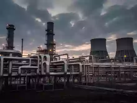 Industriepark mit komplexem Rohrleitungssystem und Kühltürmen in der Dämmerung - Foto: über boerse-global.de