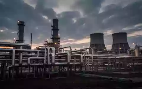 Industriepark mit komplexem Rohrleitungssystem und Kühltürmen in der Dämmerung - Foto: über boerse-global.de