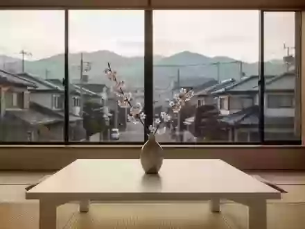 Ein minimalistischer japanischer Wohnraum mit Kirschblütenzweig in einer Vase auf einem Holztisch vor einem Fenster. - Foto: über boerse-global.de