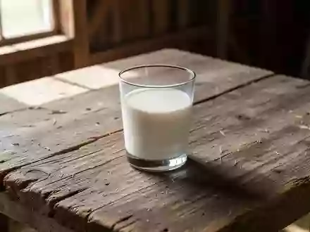 Ein einzelnes Glas frische Milch auf einem rustikalen Holztisch in einem hellen, sonnendurchfluteten Raum. - Foto: über boerse-global.de
