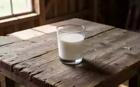 Ein einzelnes Glas frische Milch auf einem rustikalen Holztisch in einem hellen, sonnendurchfluteten Raum. - Foto: über boerse-global.de